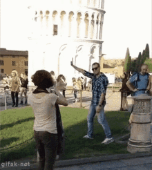 a woman is taking a picture of a man standing in front of a building with gifak.net at the bottom