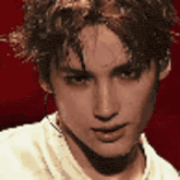 a close up of a young man 's face with a red background and a white shirt .