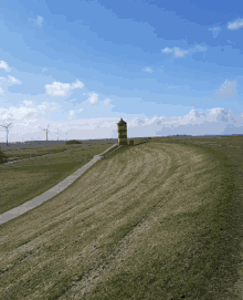 a tower sits on top of a grassy hill in the middle of a field with windmills in the background