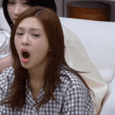 a woman in a plaid shirt is yawning on a couch