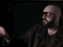 a bald man with a beard wearing sunglasses and a leather jacket is standing in a dark room .