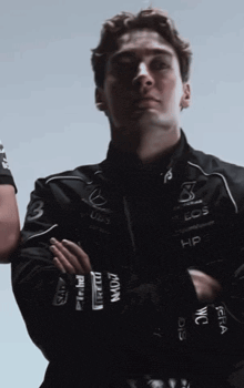 a man with his arms crossed is wearing a jacket that says petronas on the sleeves