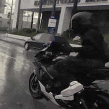 a man is riding a motorcycle down a wet street in front of a building that has the word bank on it