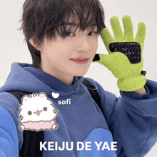 a person wearing a blue hoodie and a green glove with the name keiju de yae on the bottom