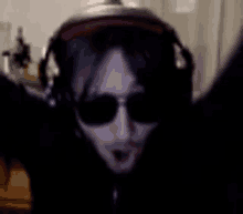 a man wearing headphones and sunglasses is standing in a dark room with his arms outstretched .