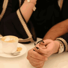 a man and a woman are holding hands in front of a cup of cappuccino