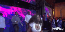 a woman is dancing in front of a large screen that says imgplay on the bottom