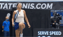 a woman in a blue skirt is holding a tennis racquet in front of a sign that says serve speed