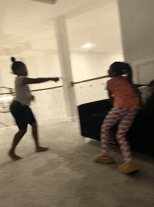 two girls are dancing in a living room in front of a couch