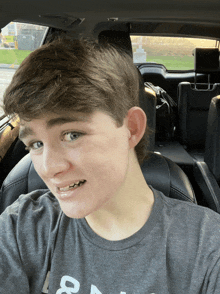 a young boy wearing a grey shirt with the letter a on it is sitting in a car