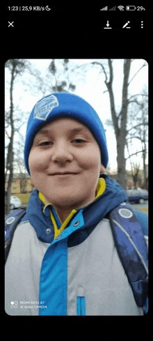 a boy wearing a blue hat and a blue jacket is smiling for the camera