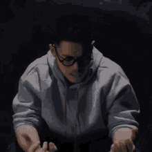 a man wearing glasses and a grey hoodie is making a gesture with his hands