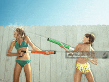 two girls in bikinis playing with water guns on a fence