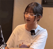 a young woman wearing glasses and a white shirt is sitting at a table .