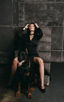 a woman in a black dress is sitting on a box next to a dog