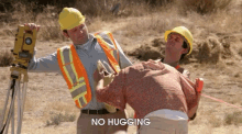 two men wearing hard hats and safety vests standing next to each other with the words " no hugging " on the bottom right