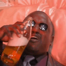 a man wearing sunglasses is drinking a beer from a glass .