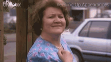 a woman in a blue floral shirt is standing in front of a car with the words keeping up appearances on the bottom