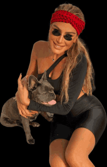 a woman wearing a red headband and sunglasses holds a dog