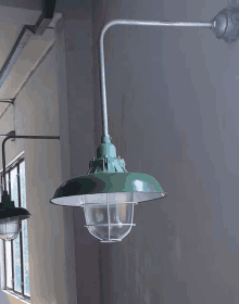 a green light with a clear glass shade is hanging from a metal pipe