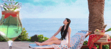 a woman in a white dress is sitting on a lounge chair near the ocean