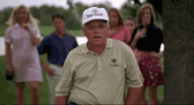 a man wearing a top-flite hat is standing on a golf course with a group of people behind him .