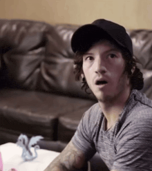 a man sitting on a couch wearing a hat and a grey shirt