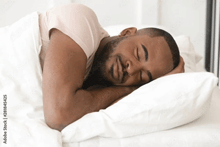 a man with a beard is sleeping in a bed with white sheets