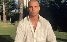 a man in a white shirt with a necklace around his neck looks at the camera