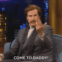 a man in a suit is sitting on a couch and giving the middle finger and says come to daddy