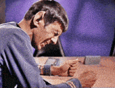 a man sitting at a table with his eyes closed and a purple background