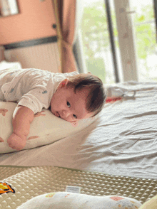 a baby is laying on a pillow on a bed looking at the camera