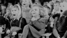 a group of children are sitting in chairs with their hands on their chests in a black and white photo .