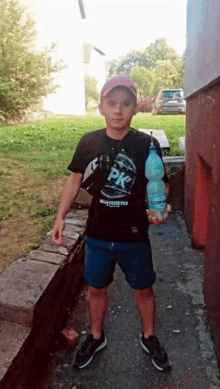 a boy wearing a pk shirt holds a large bottle of water