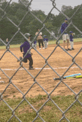 a little boy in a purple shirt is running on a baseball field with a chain link fence in the foreground