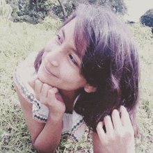 a young girl is laying in the grass with her hands on her face and smiling .