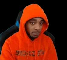 a man wearing an orange hoodie is sitting in a chair and making a funny face .