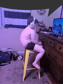 a boy wearing headphones sits on a yellow stool in front of a computer