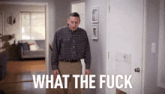 a man in a plaid shirt stands in a hallway with the words what the fuck written on the door