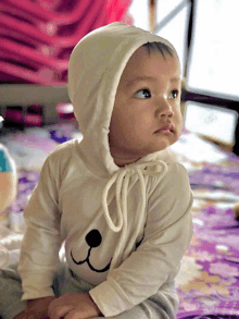 a baby wearing a white hooded top with a bear face on it