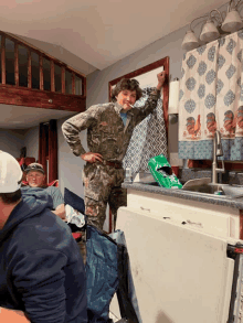 a man in a camo uniform is standing in a kitchen with other people