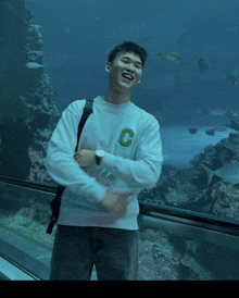 a man wearing a white sweatshirt with the letter c on it smiles in front of an aquarium