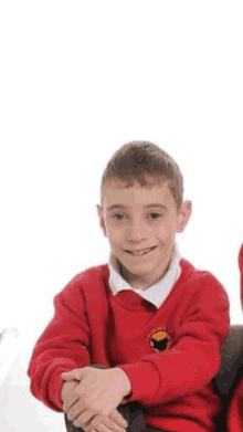 a young boy in a red school uniform is sitting down with his hands folded .