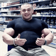 a man in a black shirt is giving a thumbs up in front of a shelf that has a bottle of whey protein