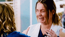 a woman in a white coat is crying while hugging another woman in a blue shirt .