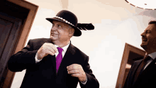 a man wearing a black hat and a purple tie stands next to another man