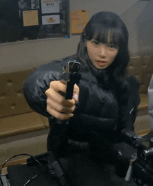 a woman in a black jacket is holding a gun in her hand