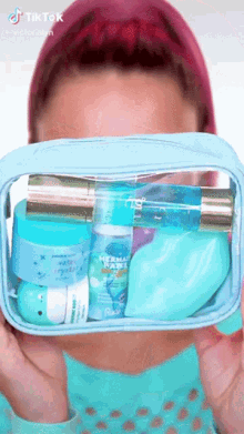 a woman is holding a clear cosmetic bag filled with various cosmetics including a lip balm