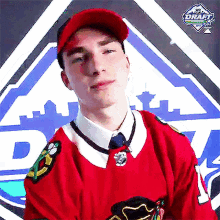 a young man wearing a red jersey and a red hat is standing in front of a sign that says draft