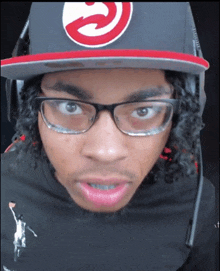 a young man wearing glasses and a hat with a red g on it